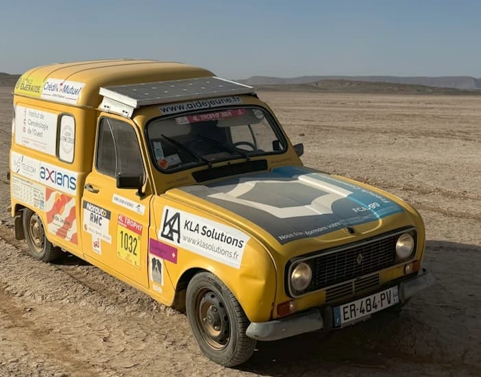 Une voiture Renault 4L jaune couverte de divers autocollants de sponsors et arborant le logo de FCA.gg sur son capot, durant l'événement 4L Trophy en 2024.