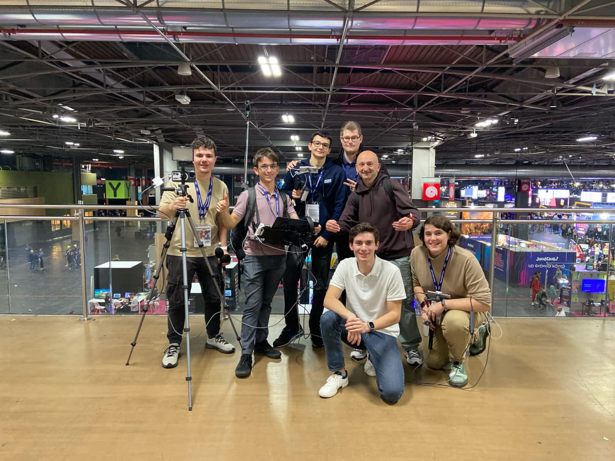 Seven of the crew posing with the filming kit, on a mezzanine overlooking the show floor.
