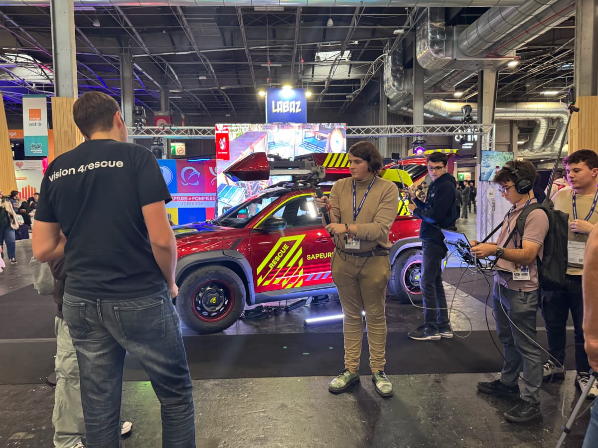 The crew filming on the Sapeurs-Pompiers de France stand, in front of a rescue vehicle.