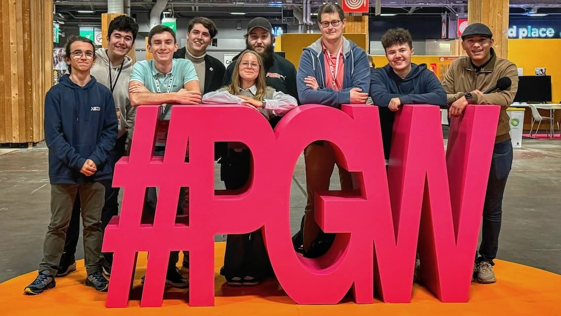 L'équipe FCA joyeuse et détendue, posant derrière une grande inscription en trois dimensions "PGW" de couleur rose vif à la Paris Games Week 2023.