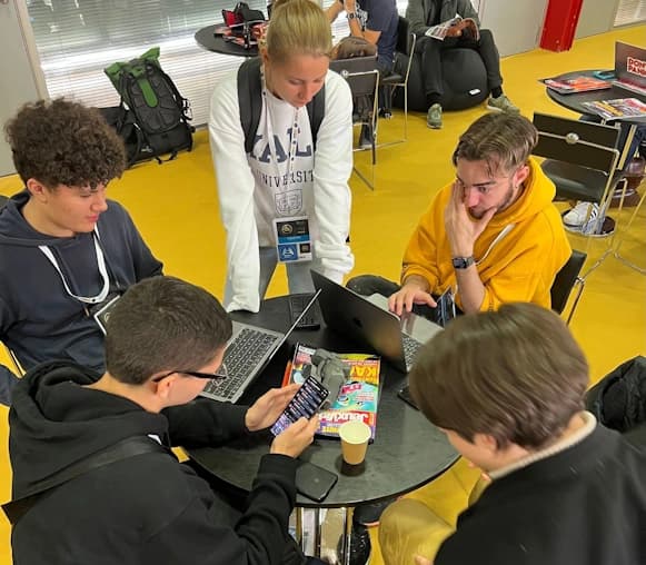Cinq membres de l'équipe FCA concentrés autour d'une petite table ronde, travaillant ensemble dans ce qui semble être un espace presse.