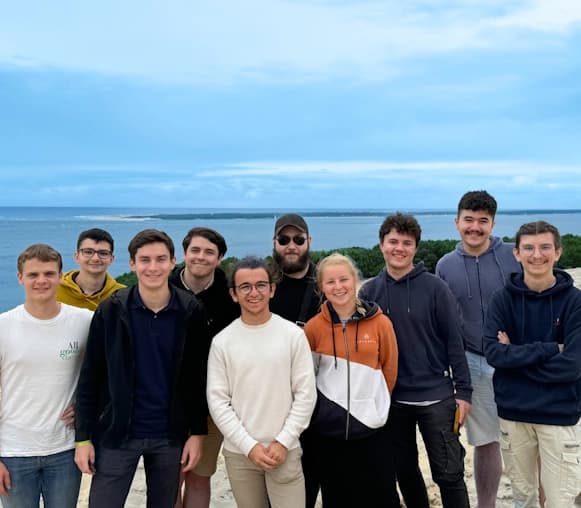Dix membres de l'équipe FCA posent ensemble sur la Dune du Pilat, avec la mer en arrière-plan sous un ciel lumineux.