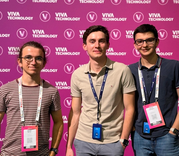 Trois membres de l'équipe FCA posent devant un mur rose vif avec le logo "Viva Technology" répété en arrière-plan. Ils portent chacun un badge autour du cou, indiquant leur participation à l'événement technologique. L'atmosphère est professionnelle et dynamique, soulignant leur présence dans un cadre axé sur l'innovation et la technologie. Ils semblent détendus et enthousiastes.